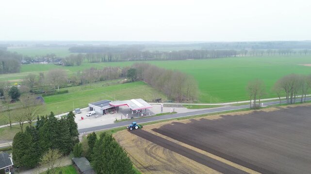 A dynamic video showing a large tractor making a sharp turn while plowing fertile land. In the background, a roadside gas station and passing cars on a highway provide a striking contrast