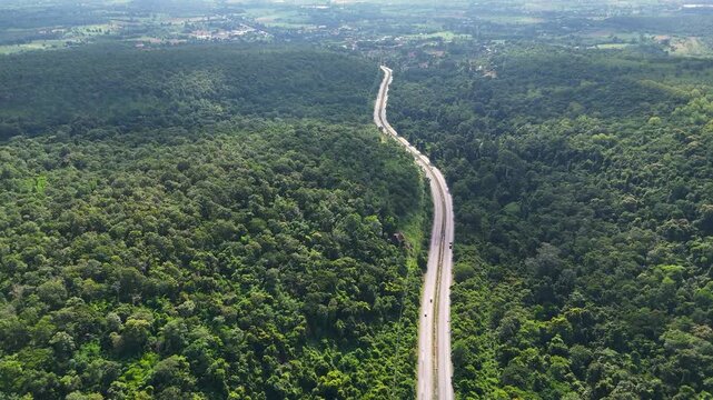 High-angle drone footage of a winding mountain road cutting through dense green forest, capturing natural landscape, scenic travel route, and peaceful countryside environment from above.
