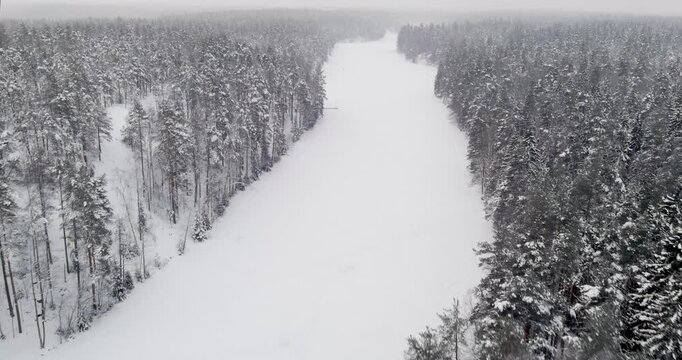 Aerial view of snow-covered landscape of frozen Kaitalampi lake winding through a dense, snow-draped boreal forest in cloudy winter weather, Espoo, Finland, Europe.