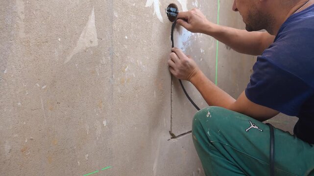 Installing Outlet With Cables Inside. Kneeling Electrician Connecting Wires To Outlet Unit. Electrician Carefully Managing Wiring And Securing Connections In Concealed Wall Cavity