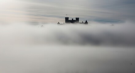 Fototapeta premium Imposing historic structure silhouette rises above dense, low-lying atmospheric moisture