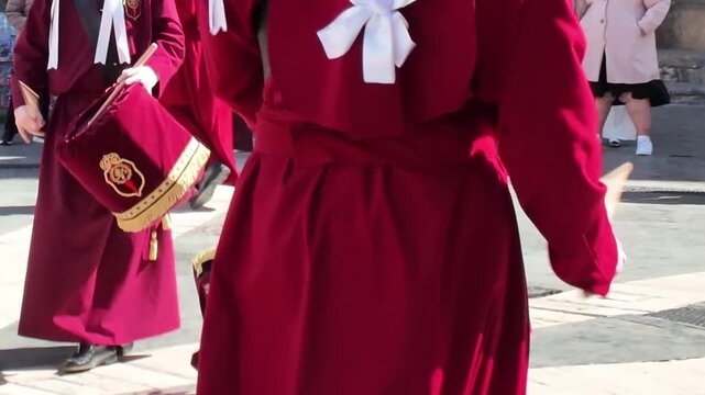 A close up back view of a person wearing a traditional red velvet tunic and white bow participating in a Murcia Semana Santa procession carrying a drum called a burlas representing the rich cultural a