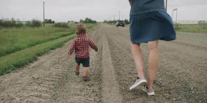 Toddler running down a dirt road with mother following behind