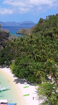 Aerial view of tropical beach with turquoise water and palm trees in El Nido, Palawan, Philippines. Popular Seven Commandos Beach with boats, white sand and vibrant island scenery.