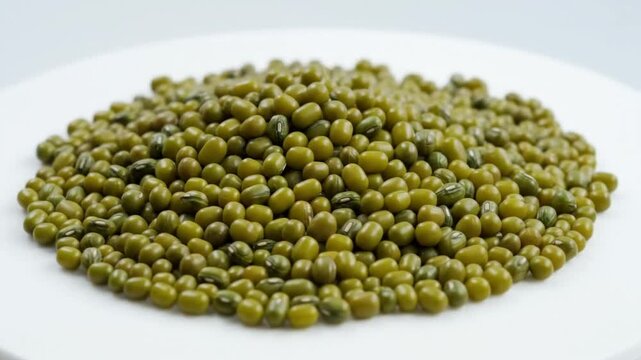 Close-up view of a heap of uncooked green mung beans on a white plate ready for cooking