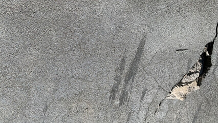 Detailed view of a weathered gray concrete wall featuring a deep, irregular crack running vertically through the rough, textured surface, showcasing urban decay and material damage. © Basit