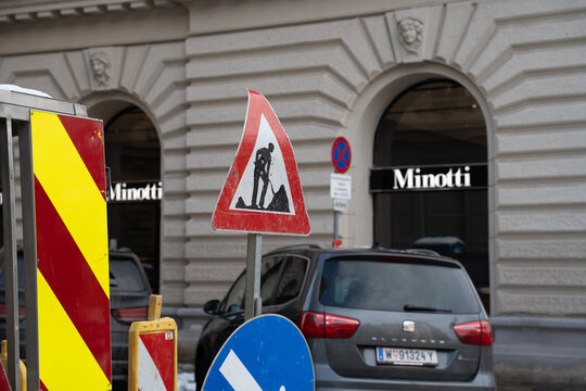 Vienna, Austria- Feb 21, 2026: Road construction signs alert pedestrians in front of Minotti store, indicating ongoing work in the urban area with parked cars nearby.