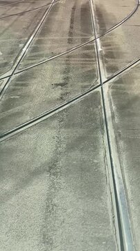 Tram rails converging on concrete junction, closeup of embedded track groove and steel rail, worn pavement textures and subtle tire marks,