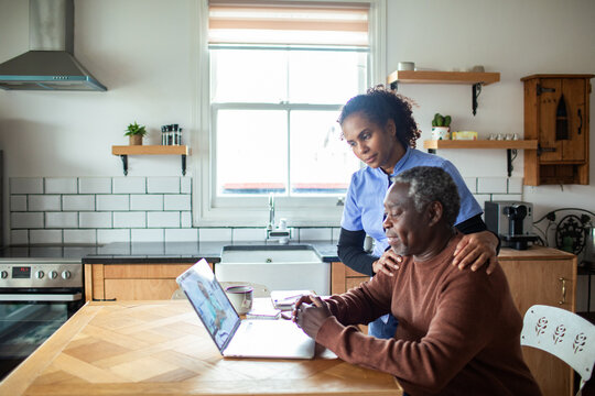 Caregiver assisting senior man with laptop at home kitchen