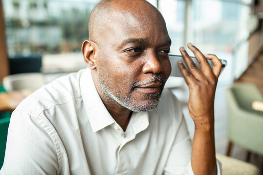 Mature man using voice assistant on smartphone at cafe