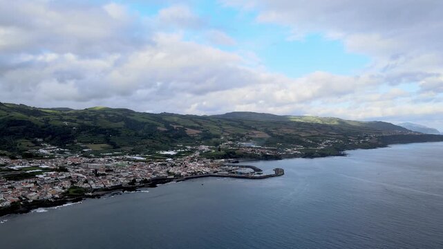 Aerial drone view of Vila Franca do Campo on S&atilde;o Miguel Island. From high altitude, the coastal town is visible with red-roof houses, agricultural fields and green landscape. The harbor and marina ext