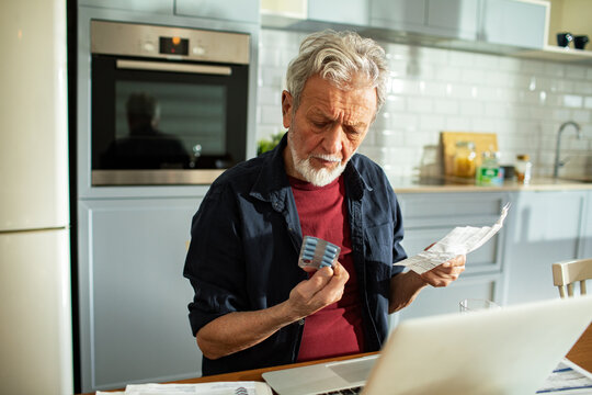 Senior man reading medication instructions at home kitchen