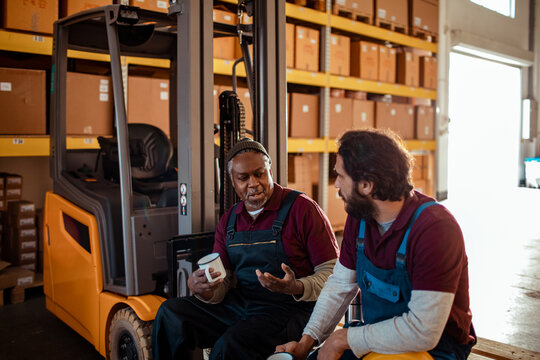Two warehouse workers taking a coffee break by forklift