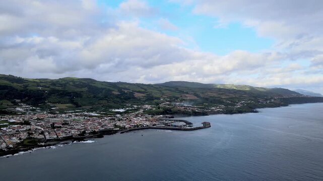 Aerial drone view of Vila Franca do Campo on S&atilde;o Miguel Island. From high altitude, the coastal town is visible with red-roof houses, agricultural fields and green landscape. The harbor and marina ext