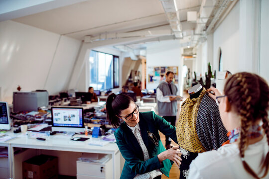 Two fashion designers adjusting dress on mannequin in open plan studio