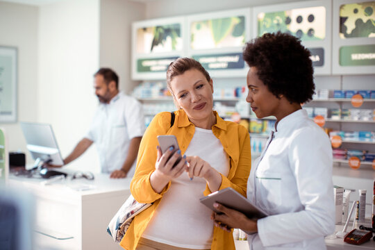 Customer consulting pharmacist about medication using smartphone in modern pharmacy