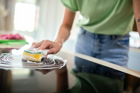 Person cleaning kitchen stovetop with soapy sponge at home