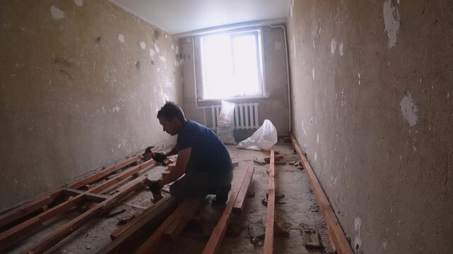 Worker Removing Damaged Flooring. Person Dismantling Decayed Wooden Flooring In Apartment. Worker Carefully Extracting Rotten Wooden Planks From Dusty Apartment Floor For Disposal