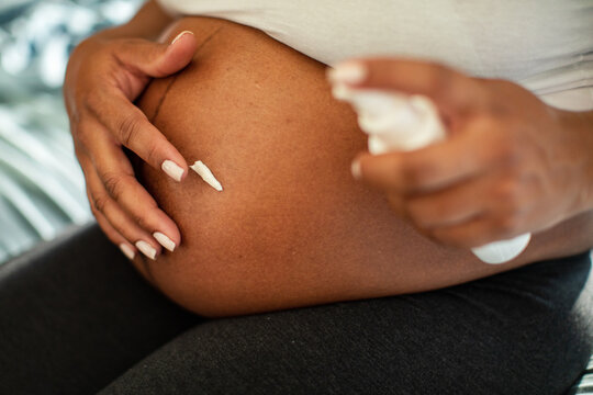 Pregnant woman applying belly cream at home