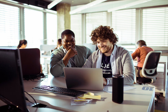 Diverse coworkers collaborating on laptop in modern office
