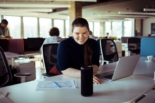 Smiling businesswoman using voice assistant in open plan office