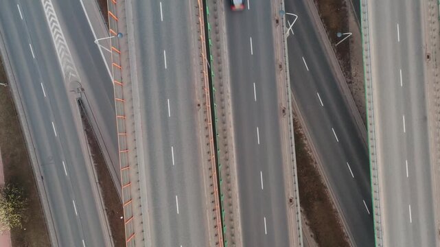 Aerial top view complex highway interchange with overpasses and multilane roads. Cars move through structured junction, forming geometric patterns. Urban transport network in daylight