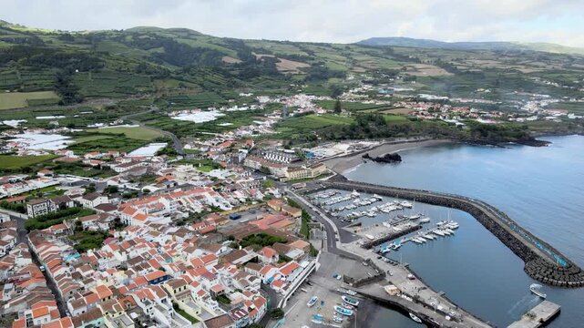 Aerial drone view of Vila Franca do Campo on S&atilde;o Miguel Island. From high altitude, the coastal town is visible with red-roof houses, agricultural fields and green landscape. The harbor and marina ext