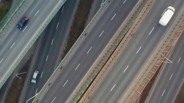 Aerial top view complex highway interchange with overpasses and multilane roads. Cars move through structured junction, forming geometric patterns. Urban transport network in daylight