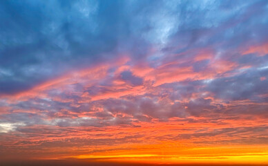 Obraz premium Stunning sunset sky filled with textured clouds glowing in shades of orange, pink, and blue, creating a dramatic and colorful natural background.