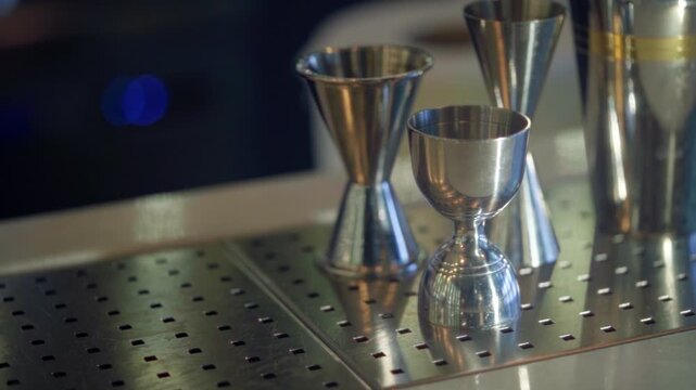 Bartender's hand picking up gold jigger from bar counter among other tools