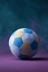 Fototapeta premium Vibrant blue and yellow soccer ball on a purple surface with smoky blue background
