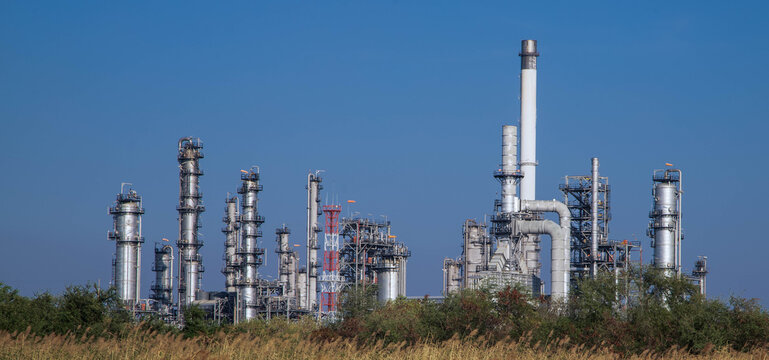 Oil and gas refinery plant with distillation columns and smokestacks under clear blue sky.