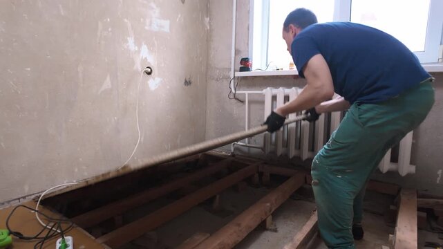 Focused man in workwear dismantling the old particle board flooring, lifting and removing a large panel to expose the wooden joists during a major home improvement and remodeling project