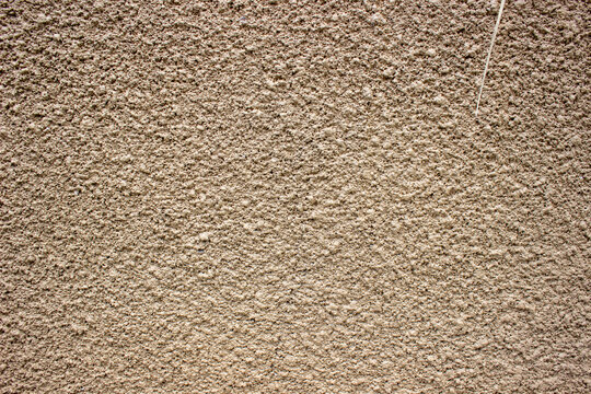 Rough light brown cream cement wall texture with prominent speckled patterns giving a minimalist industrial impression to the building facade.