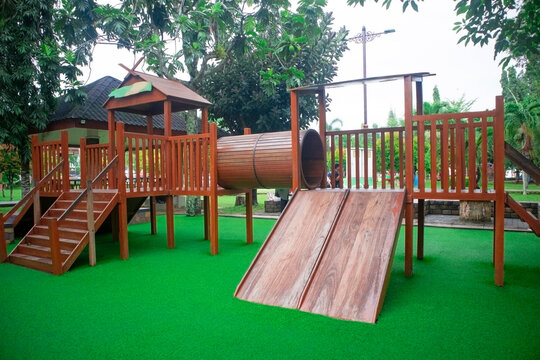 Wooden playground structure with stairs and slides on green artificial grass in a public park