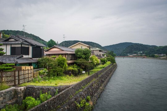 Traditional and modern residential houses built along a stone river embankment in a peaceful mountain valley in Japan.