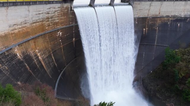 Curved Concrete Dam Spillway Releasing Powerful Torrent Of Water Into Misty Basin - Eume Reservoir, Galicia, Spain. aerial shot