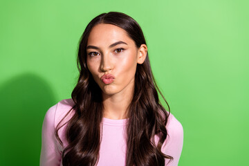Fototapeta premium Young woman in pink shirt kissing lips posing against bright green background for fashion and lifestyle stock photo