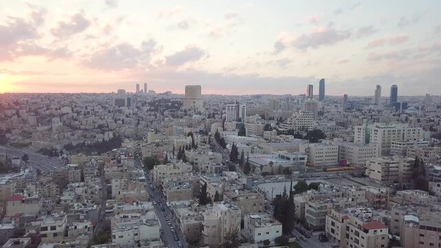 Cinematic aerial view of Amman city skyline during golden hour sunset with birds flying over urban landscape