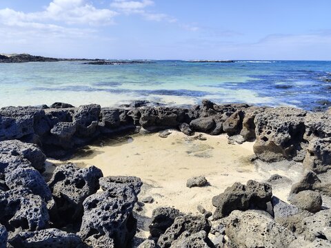 Natural volcanic rock pool on a sandy beach with blue sky and turquoise sea in Fuerteventura Canary Islands. 