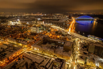 Naklejka premium Aerial night view of Kyiv's Podil district and illuminated bridges in winter.