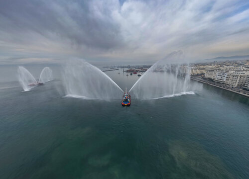 Panoramic aerial view of a fireboat performing a water salute in the port of Thessaloniki, Greece.