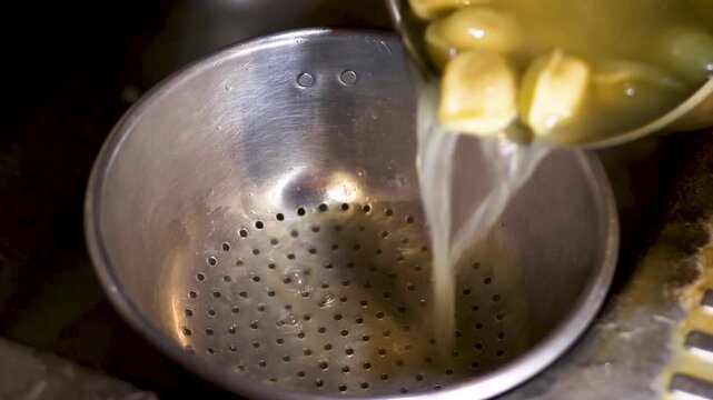 Liquid pours into strainer then dumplings settle within metal bowl