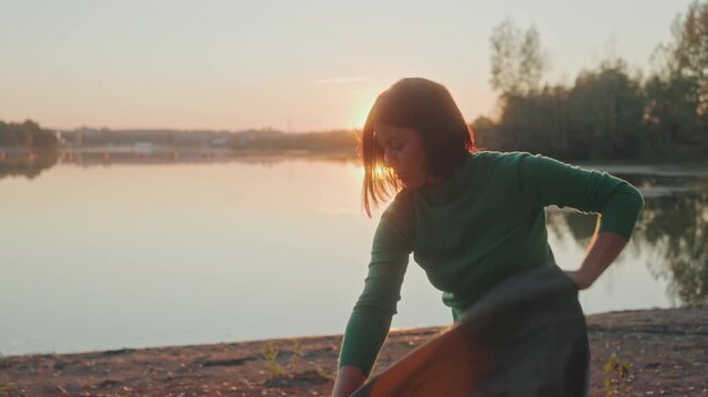 Lakeside caucasian woman pitching tent, solo camper unfolds fabric and secures poles at golden hour with a warm smile, sunlight backlighting profile and reflecting on calm water while she confidently