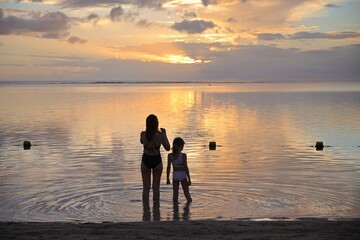 Fototapeta premium mom and daughter taking photo of sunset on the beach