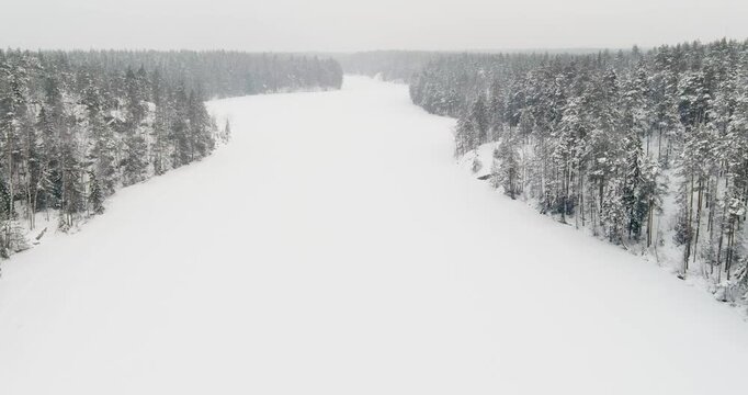 Aerial view of snow-covered landscape of frozen Kaitalampi lake winding through a dense, snow-draped boreal forest in cloudy winter weather, Espoo, Finland, Europe.