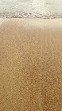 Ocean wave washing over golden yellow sand on a tropical beach, vertical video close-up of sea tide motion.