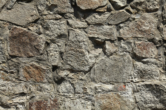 Grey granite wall, texture background. Surface of stone structure built of granite rocks (bricks). Dirty wall of volcanic grey color. Covering of large gray stones on cement base in rays of the sun