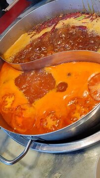 Close-up of a two-flavor metal pot with spicy malatang and tomato broth boiling. Action shot of a slice of raw beef being dipped into a bubbling Sichuan hot pot with chopsticks. 