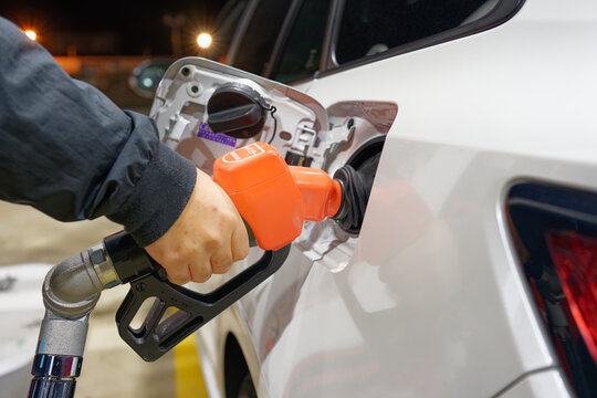 Hand refueling a white car at a gas station in Japan, concept of rising gasoline prices and household budget protection